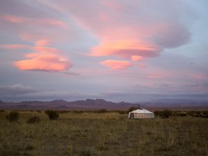 Mongolian yurt in a field beneath a sunrise.